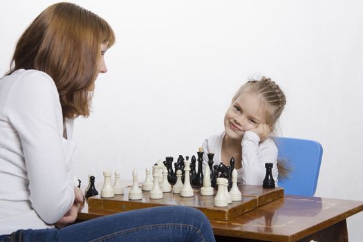 Mother and four-year-old daughter sitting at a table and play chess. Mom tells about the shapes