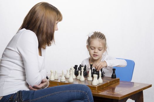 Mother and four-year-old daughter sitting at a table and play chess. Mom tells about the shapes