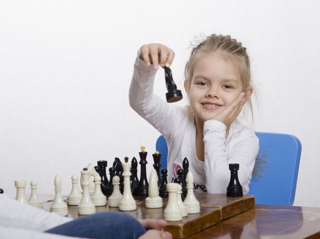 Four-year-old girl playing in chess. Girl fun looking into the frame with the figure in hand, preparing to make a move
