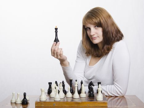 Young girl playing chess. A girl holds the shape of the Queen and looks in a frame