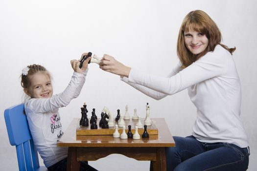 Mom and daughter playing at a table in chess. Mother teaches daughter game. They are fun to hit a few of the pieces together