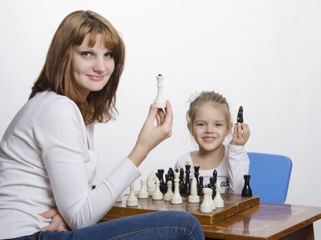 Mother and four-year-old daughter sitting at a table and play chess. Mom tells about the shapes