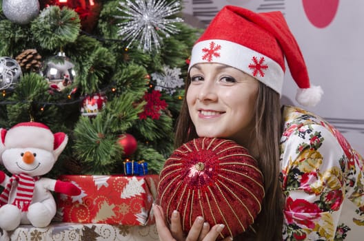 The girl lying on the carpet around the Christmas tree. In the hands of her big red Christmas ball. Girl dreams