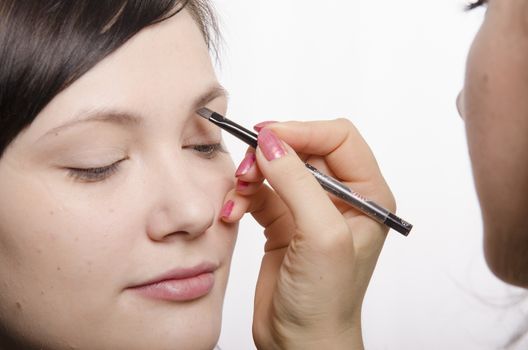 Makeup artist deals makeup on the model's face. She leads eyebrow pencil model.