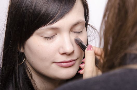 Makeup artist in the process of makeup, does the powder on the face of a beautiful girl. The girl looks frame