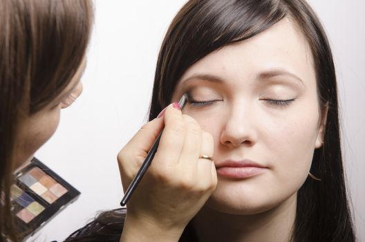 Makeup artist deals makeup on the model's face. She paints the shadows of the upper eyelids model.