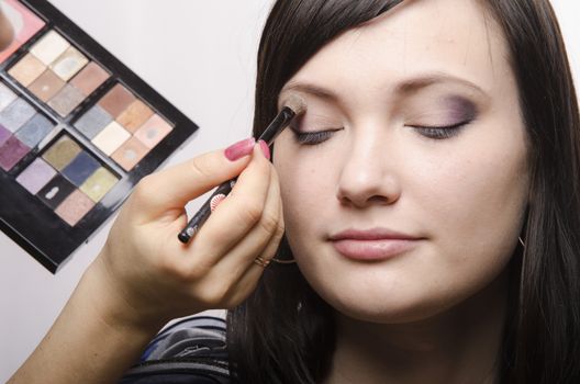 Makeup artist deals makeup on the model's face. She paints the shadows of the upper eyelids model.