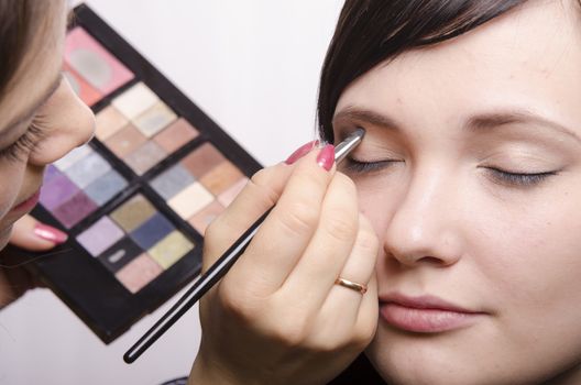 Makeup artist deals makeup on the model's face. She paints the shadows of the upper eyelids model.