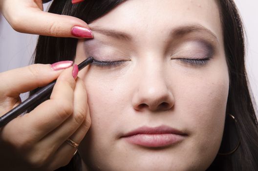 Makeup artist deals makeup on the model's face. She paints the shadows of the upper eyelids model.