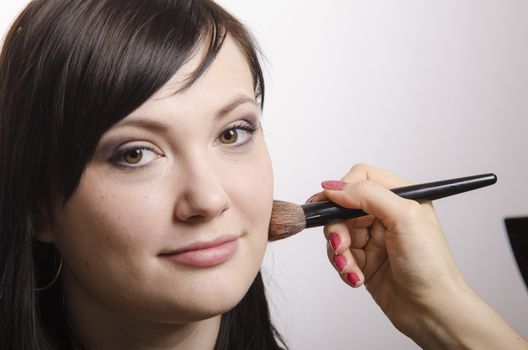 Makeup artist in the process of makeup, does the powder on the face of a beautiful girl. The girl looks frame