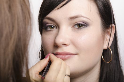 Makeup artist puts makeup beautiful girl. She paints her lips model
