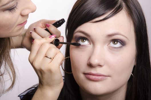 Makeup artist deals makeup on the model's face. She paints eyelashes model.
