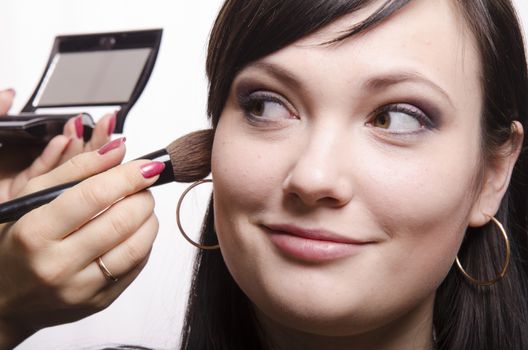 Makeup artist in the process of makeup, does the powder on the face of a beautiful girl. The girl looks frame