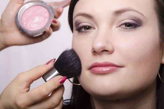 Makeup artist in the process of makeup, does the powder on the face of a beautiful girl. The girl looks frame