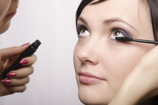 Makeup artist deals makeup on the model's face. She paints eyelashes model.