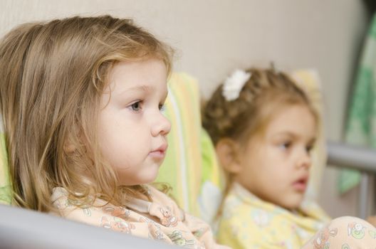 Two small children sit on the couch and enthusiastically watching the TV behind the scenes right