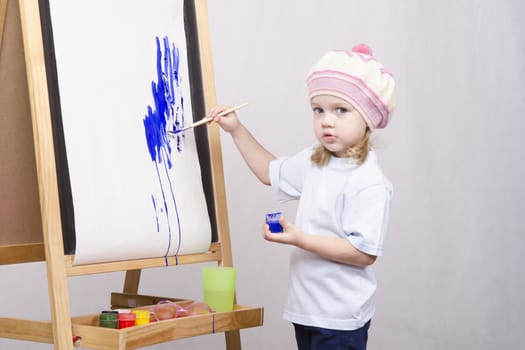 Three-year-old girl playing in the artist. Girl draws on the easel paints