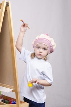 Three-year-old girl playing in the artist. Girl draws on the easel paints