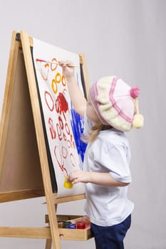 Three-year-old girl playing in the artist. Girl draws on the easel paints