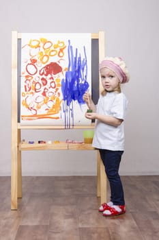 Three-year-old girl playing in the artist. Girl draws on the easel paints