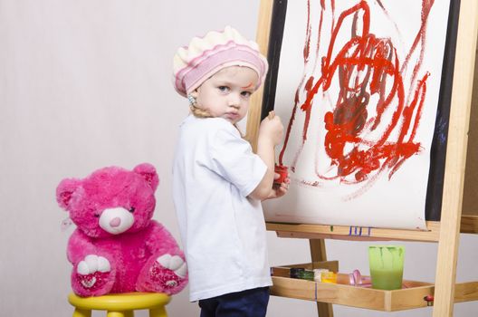 Three-year-old girl playing in the artist. Girl draws on the easel paints bear sitting on a chair