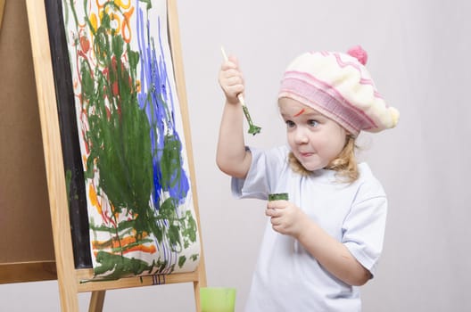 Three-year-old girl playing in the artist. Girl draws on the easel paints