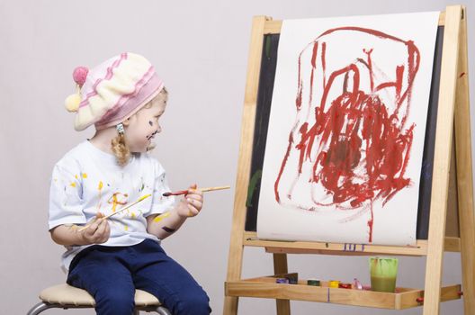 Portrait of a three-year old girl playing in the artist. Girl mud paints. Standing behind you easel