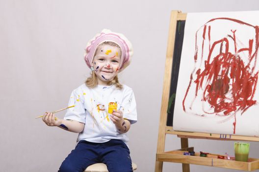 Portrait of a three-year old girl playing in the artist. Girl mud paints. Standing behind you easel