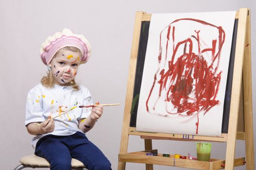 Portrait of a three-year old girl playing in the artist. Girl mud paints. Standing behind you easel