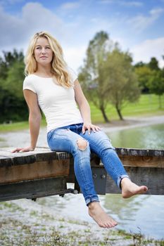 Young blond woman is sitting on a jetty at a lake in summer