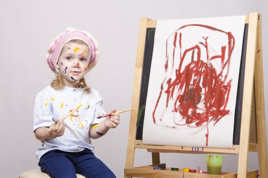 Portrait of a three-year old girl playing in the artist. Girl mud paints. Standing behind you easel