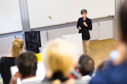 Speaker giving presentation in lecture hall at university. Participants listening to lecture and making notes.