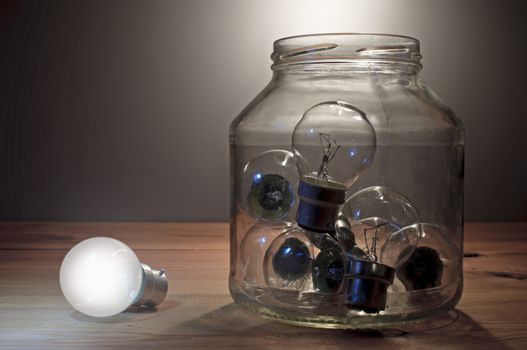 Lit bulb next to a glass jar of unlit lamps