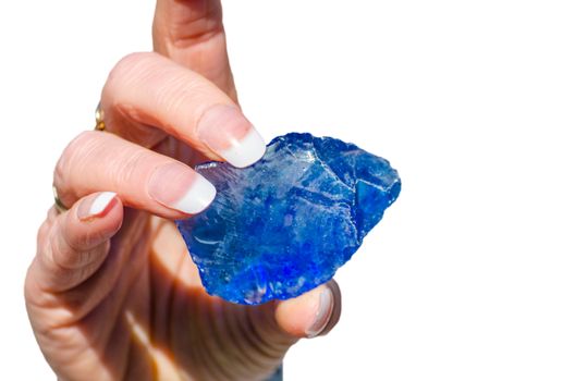 Quartz stone, glass stone pieces in blue held by a hand against white background
