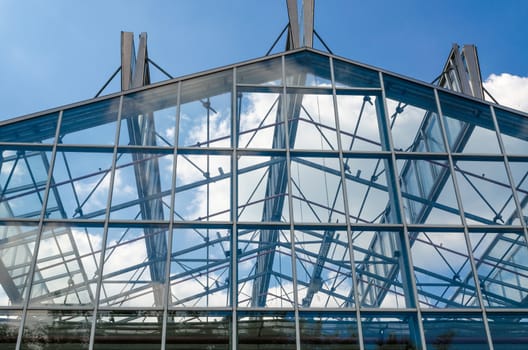 Glass roof in a steel structure against a blue sky with clouds.
