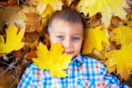 Portrait of Adorable cute boy lying on leaves in the beautiful  autumn park