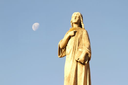 Statue in the Cemetery of Recoleta with the Moon in the background, Buenos Aires, Argentina.