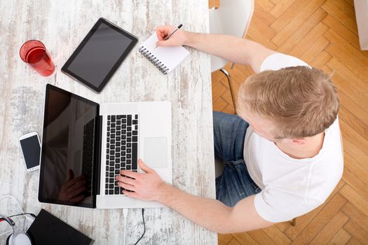 A young caucasian man working in his home office seen from above.
