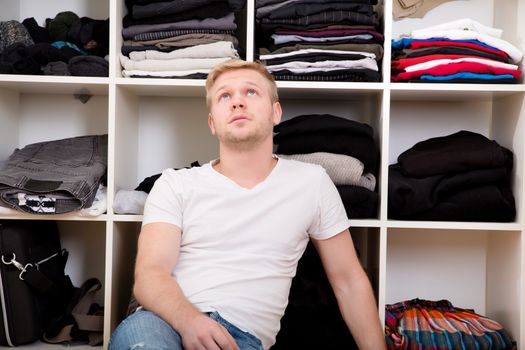 Young man sitting in front of his wardrobe	.
