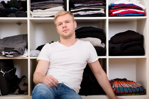 Young man sitting in front of his wardrobe	.
