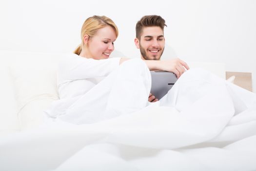 A young and happy couple with a Tablet PC  in Bed.
