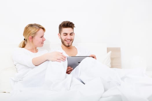 A young and happy couple with a Tablet PC  in Bed.
