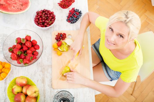 A beautiful mature woman preparing a smoothie or juice with fruits in the kitchen.
