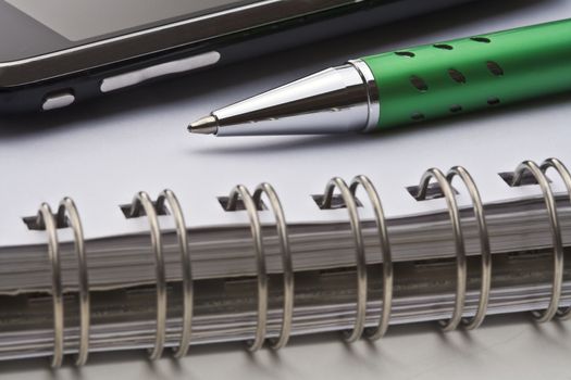 extreme closeup of a ballpoint pen, spiral notebook and cell phone