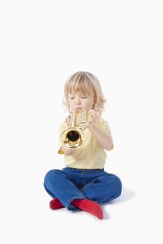 boy with long blond hair playing with toy trumpet