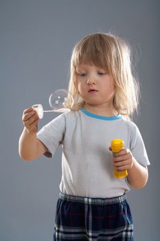 boy with long blond hair looking at big soap bubble - isolated on gray