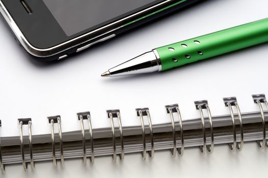 extreme closeup of a ballpoint pen, spiral notebook and cell phone