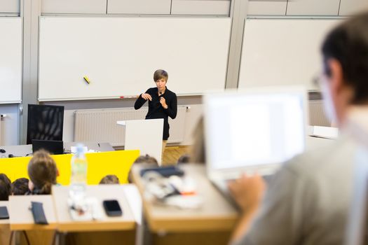 Speaker giving presentation in lecture hall at university. Participants listening to lecture and making notes.