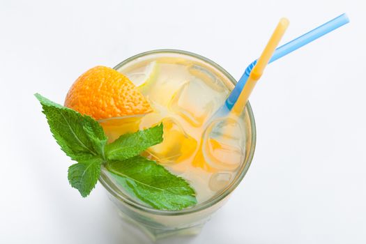 Glass of fresh made non-alcoholic drink citrus lemonade with ice cubes, mint , orange segment and straws. Top view on white background