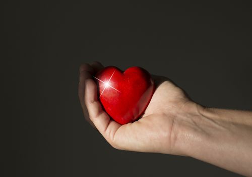 red heart shining in womans hand on dark background